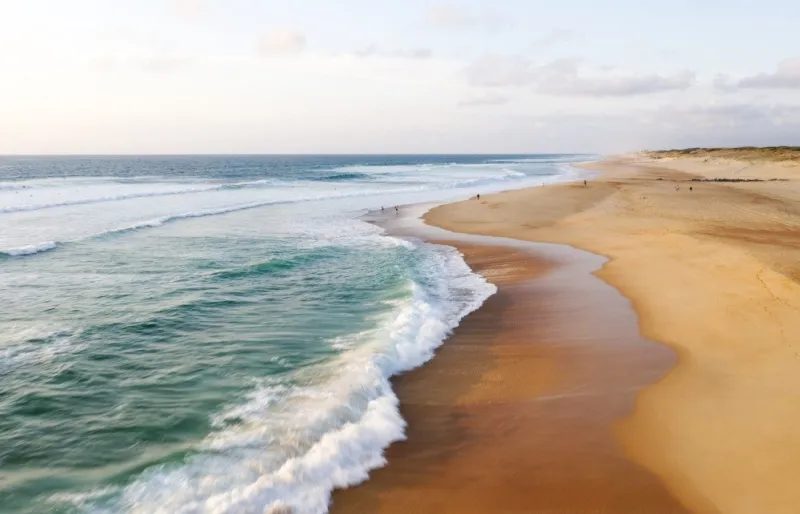 Une longue plage de sable doré entre l'océan et la dune, au coucher du soleil