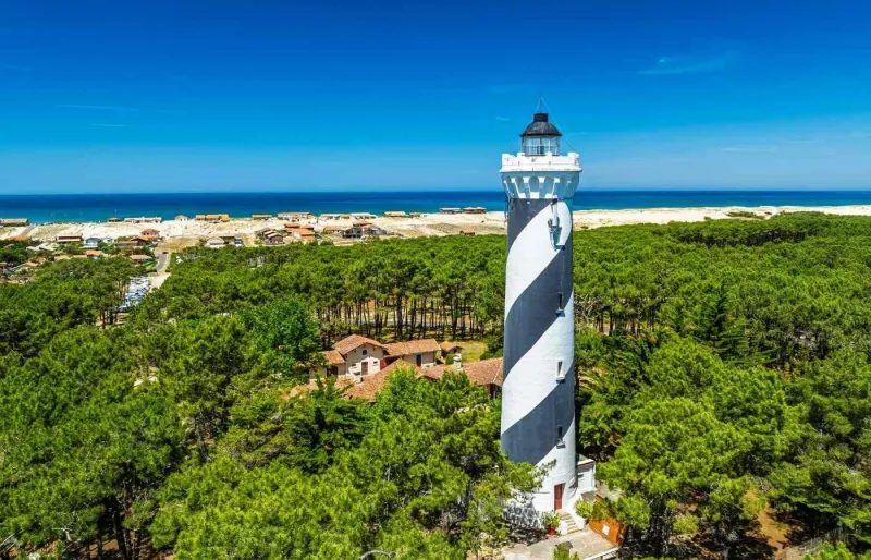 Le phare noir et blanc de Contis au milieu de la forêt de pins, l'océan à l'horizon